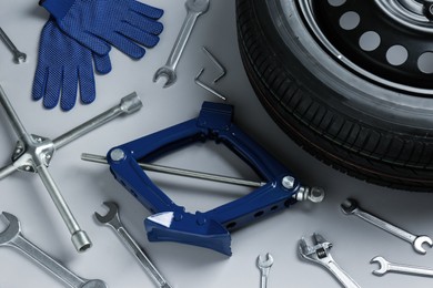 Photo of Car wheel, scissor jack, gloves and different tools on grey background, flat lay