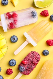 Photo of Different fruit ice pops on light yellow background, flat lay