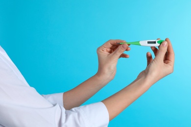 Photo of Female doctor holding digital thermometer on color background, closeup. Medical object