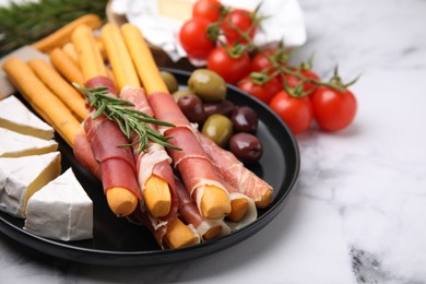 Photo of Delicious grissini sticks with prosciutto and ingredients on white marble table, closeup. Space for text