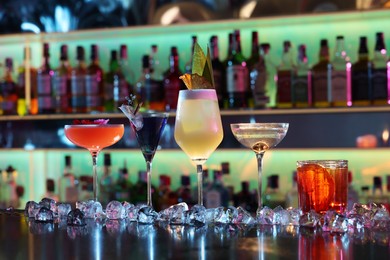 Photo of Different fresh alcoholic cocktails and ice cubes on counter in bar
