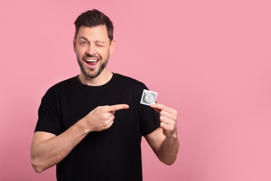 Photo of Happy man holding condom on pink background. Space for text