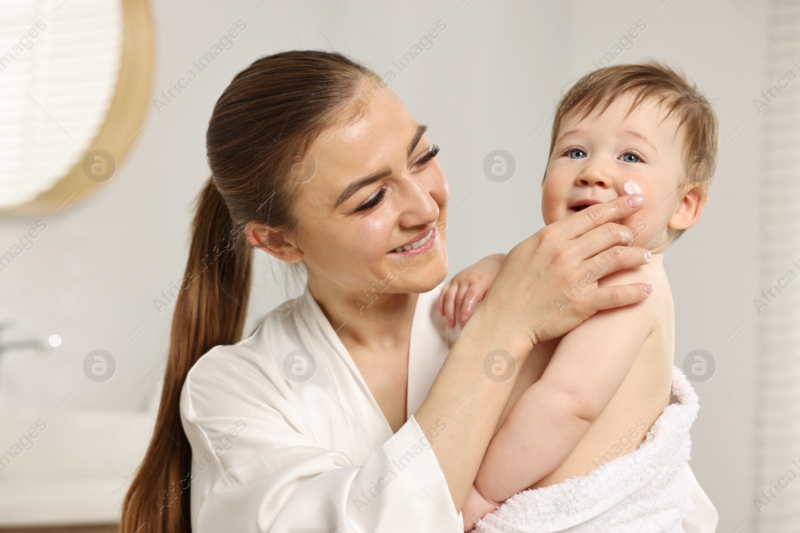 Photo of Happy mother applying moisturizing cream onto baby`s face at home