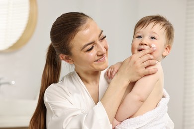 Happy mother applying moisturizing cream onto baby`s face at home