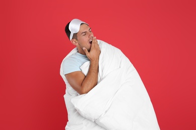 Man wrapped in blanket yawning on red background