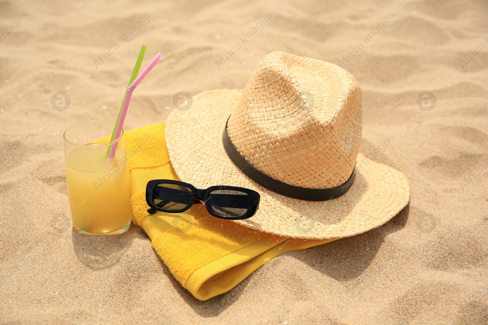 Photo of Straw hat, sunglasses, towel and refreshing drink on sand. Beach accessories