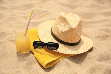 Photo of Straw hat, sunglasses, towel and refreshing drink on sand. Beach accessories