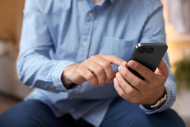 Man sending message on smartphone indoors, closeup