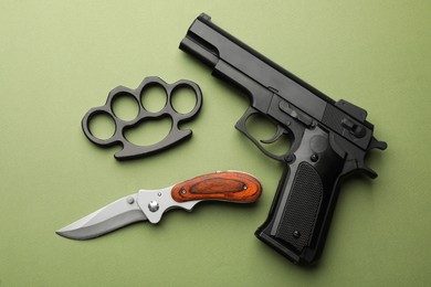 Photo of Black brass knuckles, gun and knife on green background, flat lay