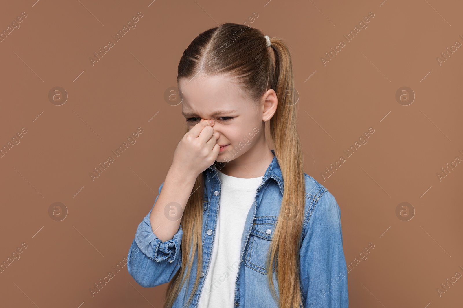 Photo of Little girl suffering from headache on brown background