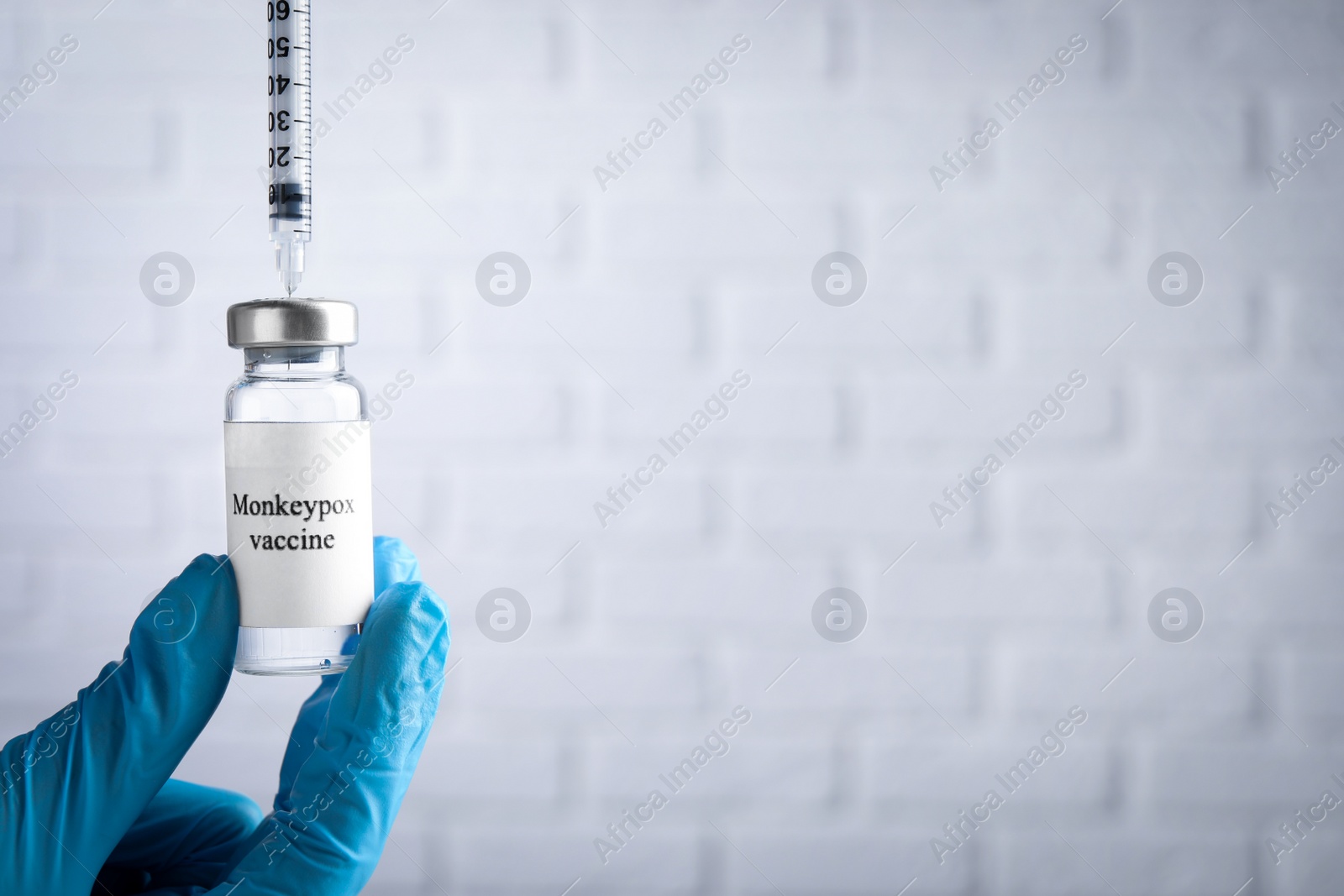 Photo of Nurse filling syringe with monkeypox vaccine from vial near white brick wall, closeup. Space for text