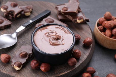Photo of Bowl with tasty paste, chocolate pieces and nuts on grey table