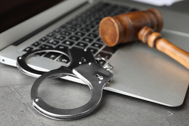 Photo of Laptop, wooden gavel and handcuffs on grey table, closeup. Cyber crime