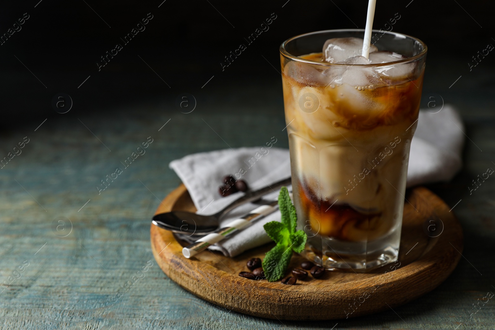 Photo of Pouring milk into glass of delicious iced coffee, mint and beans on light blue wooden table, space for text