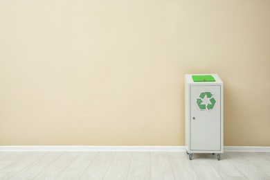 Photo of Trash bin with recycling symbol near color wall indoors. Space for text