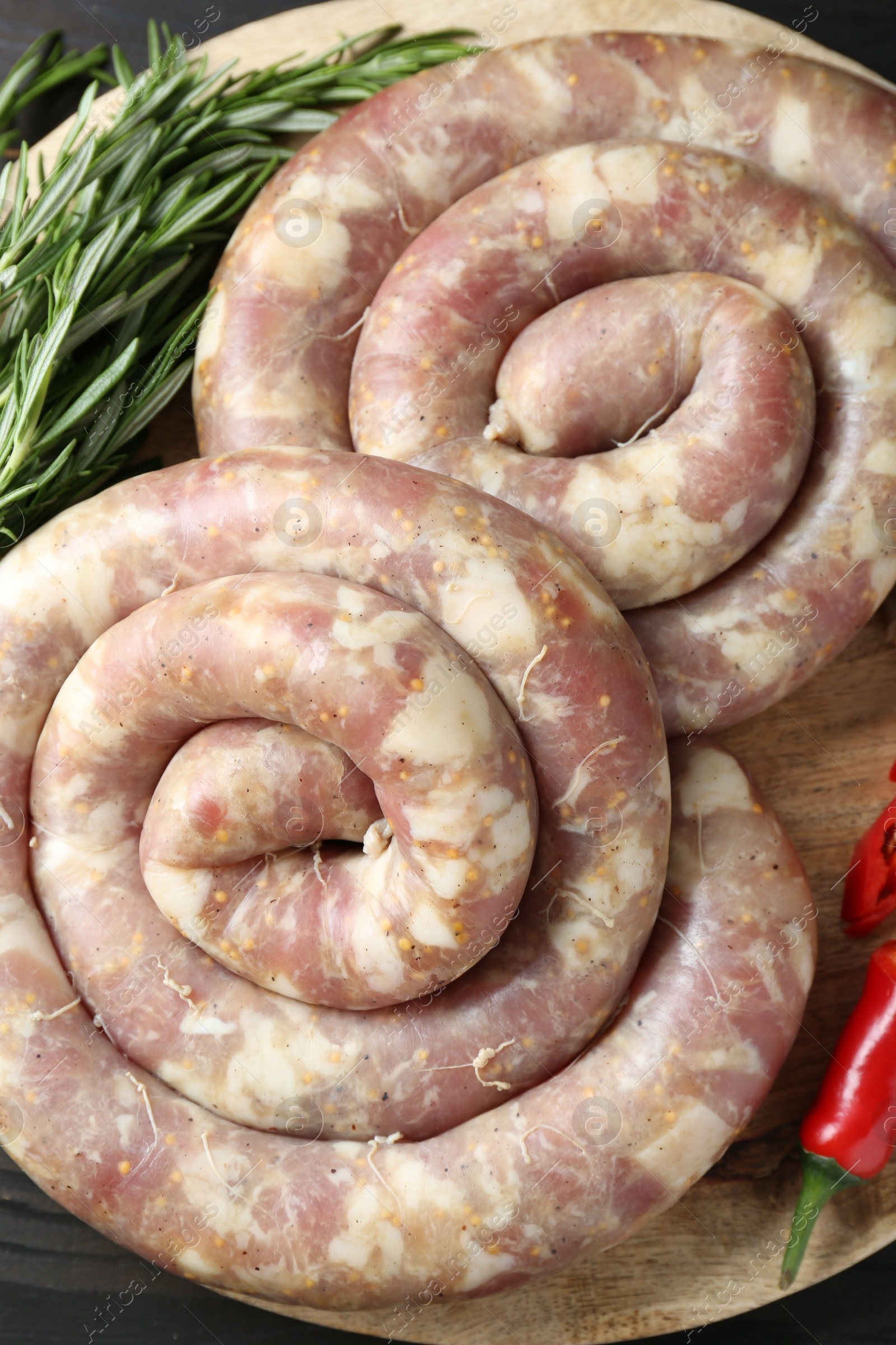 Photo of Raw homemade sausage, chili pepper and rosemary on wooden board, top view