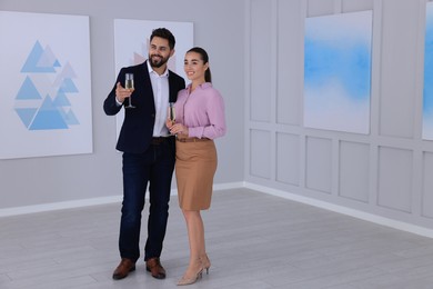 Photo of Young couple with glasses of champagne at exhibition in art gallery