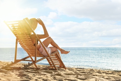 Woman relaxing on deck chair at sandy beach. Summer vacation