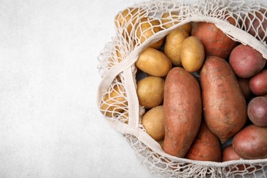 Photo of Different types of fresh potatoes in net bag on white table, top view. Space for text