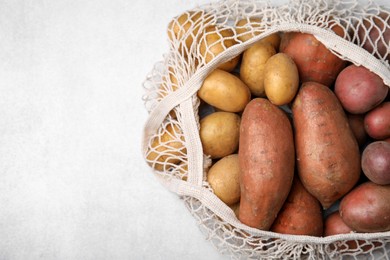 Different types of fresh potatoes in net bag on white table, top view. Space for text