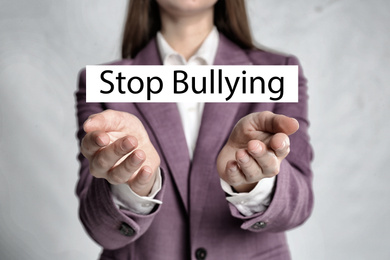 Image of Young woman showing sign STOP BULLYING on light background, closeup