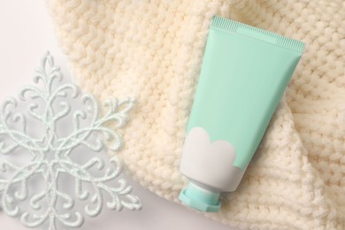Winter skin care. Hand cream, decorative snowflake and knitted sweater on white background, flat lay