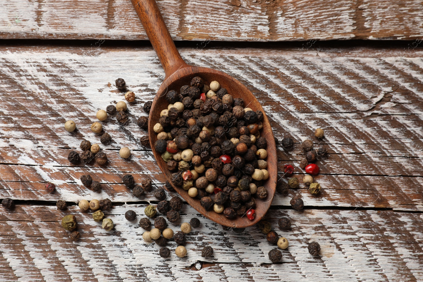 Photo of Aromatic spice. Different peppers in spoon on wooden table, top view