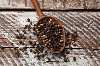 Photo of Aromatic spice. Different peppers in spoon on wooden table, top view