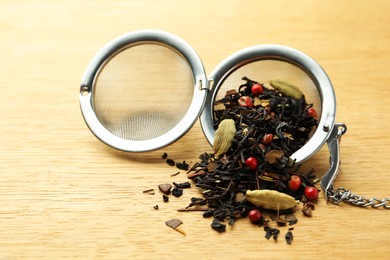 Snap infuser with dried herbal tea leaves on wooden table, closeup