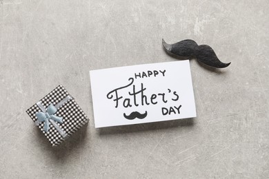 Photo of Card with phrase Happy Father's Day, paper mustache and gift box on light background, flat lay