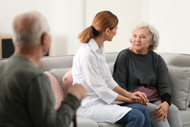 Elderly spouses with female caregiver in living room