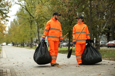 Photo of Street cleaner with brooms and garbage bags outdoors on autumn day