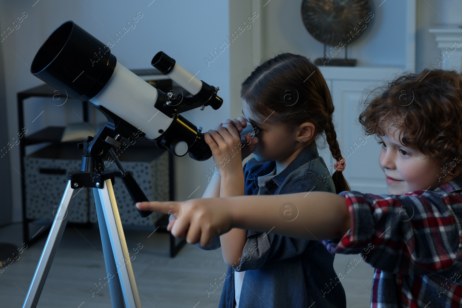 Photo of Cute little children using telescope to look at stars in room