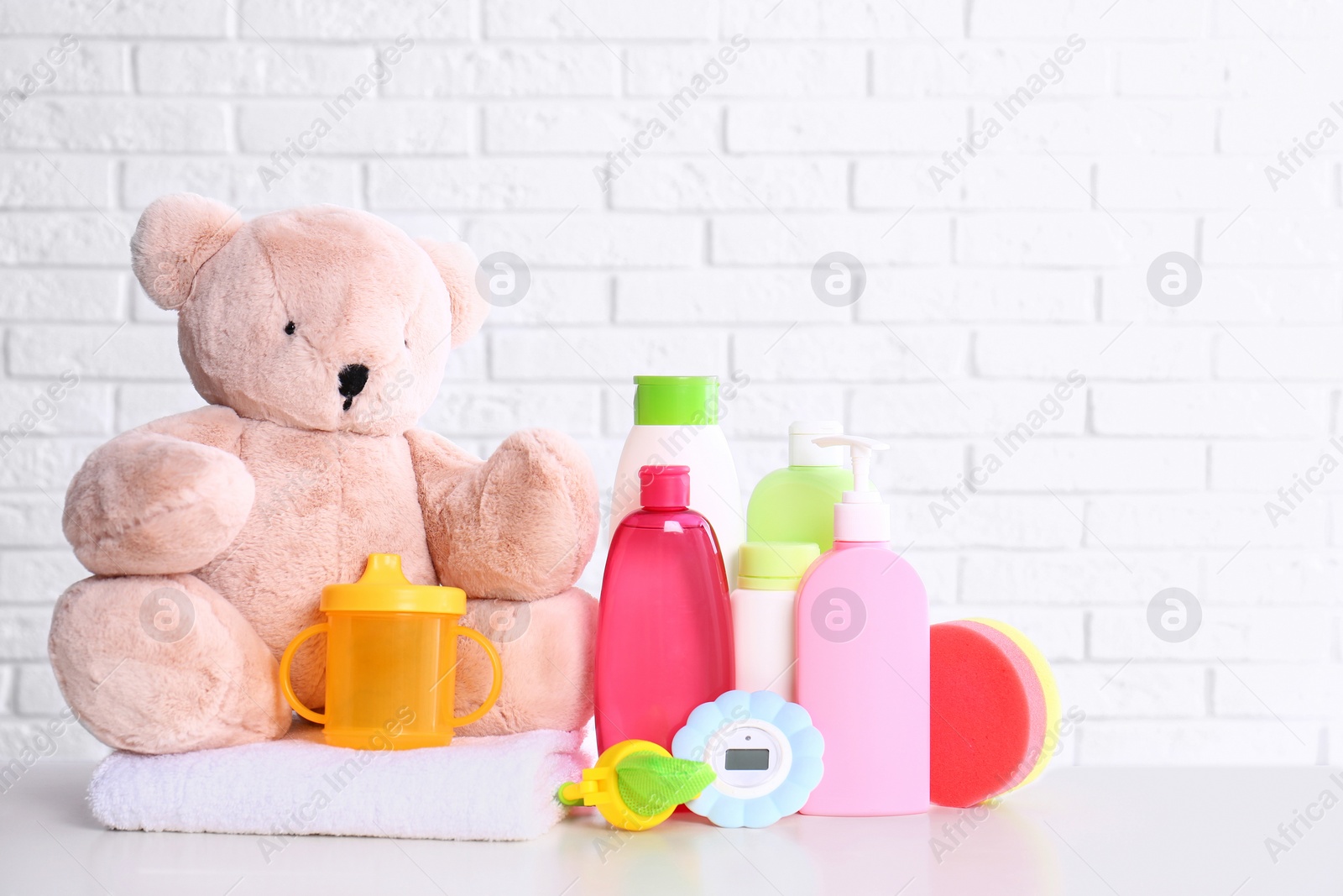 Photo of Baby accessories on table near white brick wall. Space for text