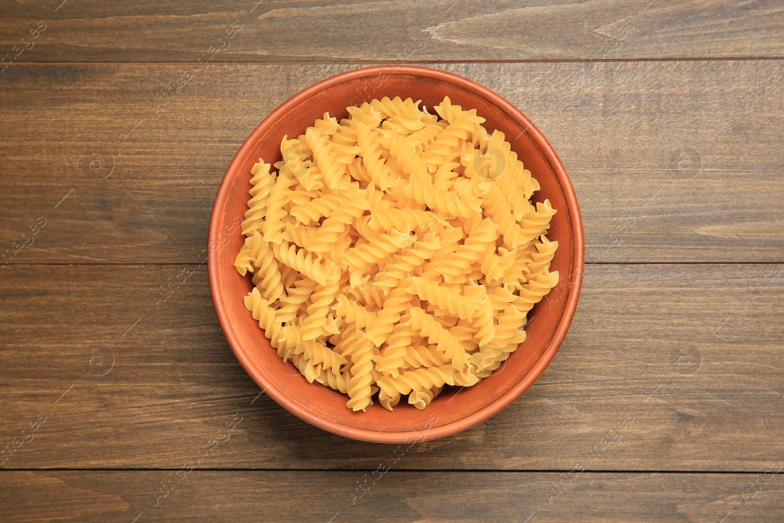 Photo of Raw fusilli pasta in bowl on wooden table, top view