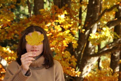 Photo of Woman holding autumn leaf against her face in forest. Space for text