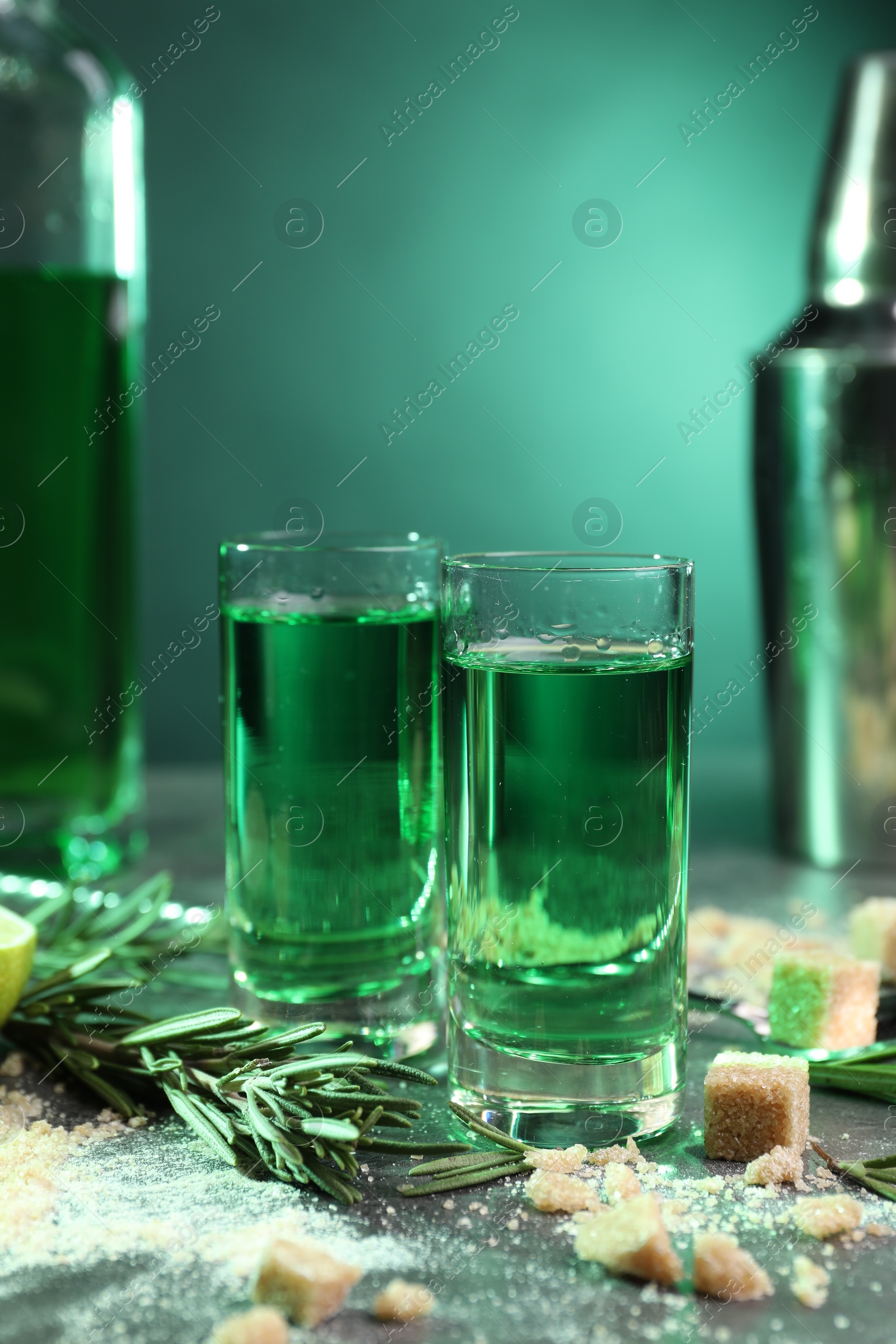 Photo of Absinthe in shot glasses, rosemary and brown sugar on table against green background. Alcoholic drink