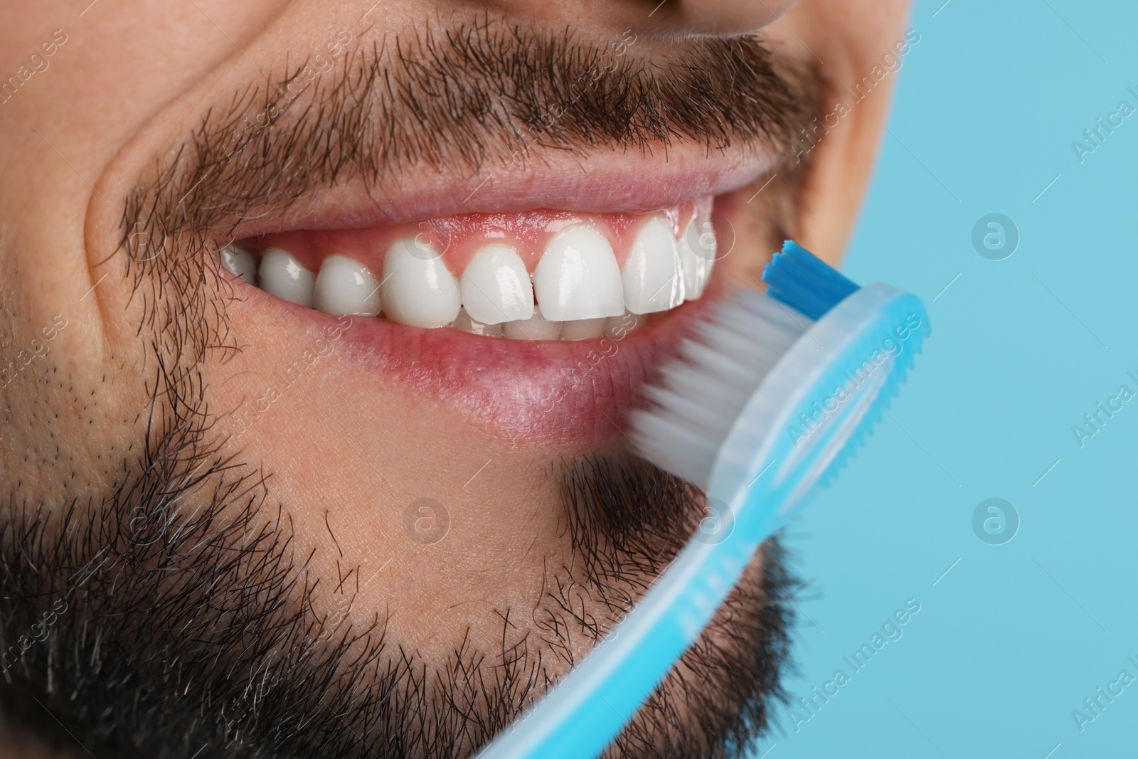 Photo of Man brushing his teeth with plastic toothbrush on light blue background, closeup