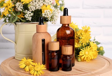 Bottles of essential oil and different wildflowers on wooden board