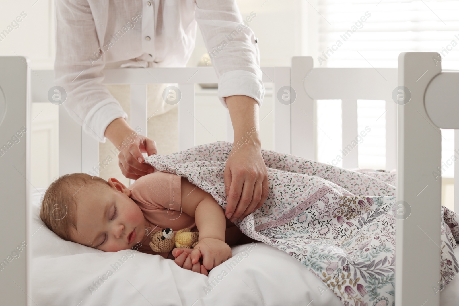 Photo of Mother covering her sleeping baby with blanket at home