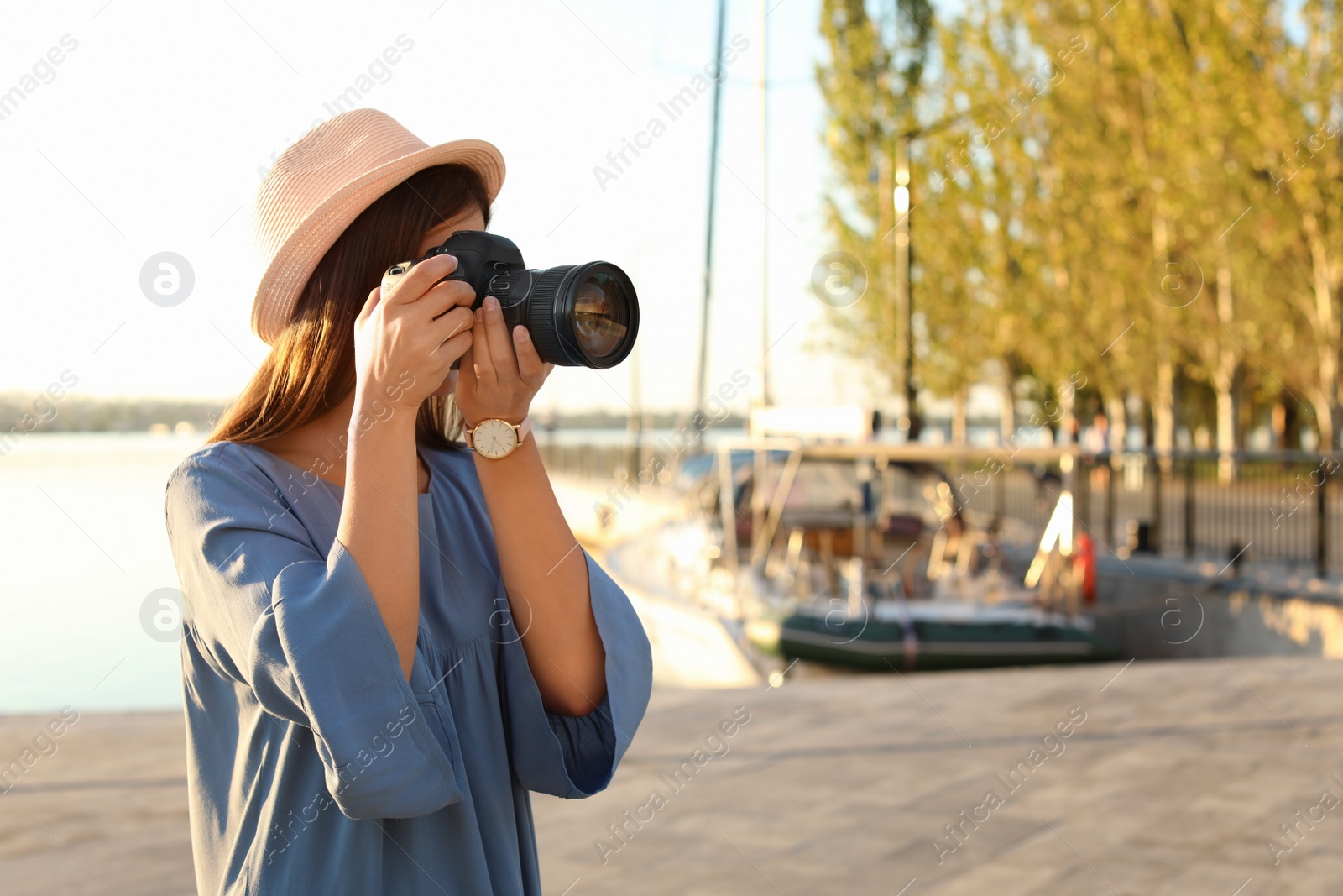 Photo of Young female photographer taking photo with professional camera at pier. Space for text