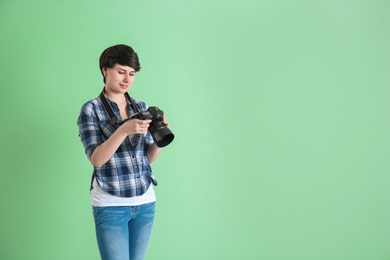 Young female photographer with camera on color background