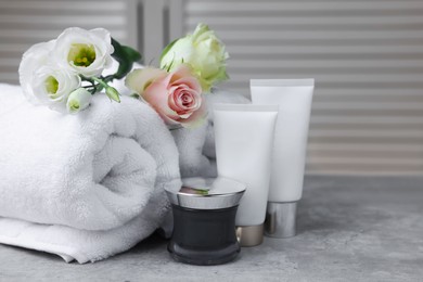 Photo of Towels, cosmetic products and flowers on grey table indoors