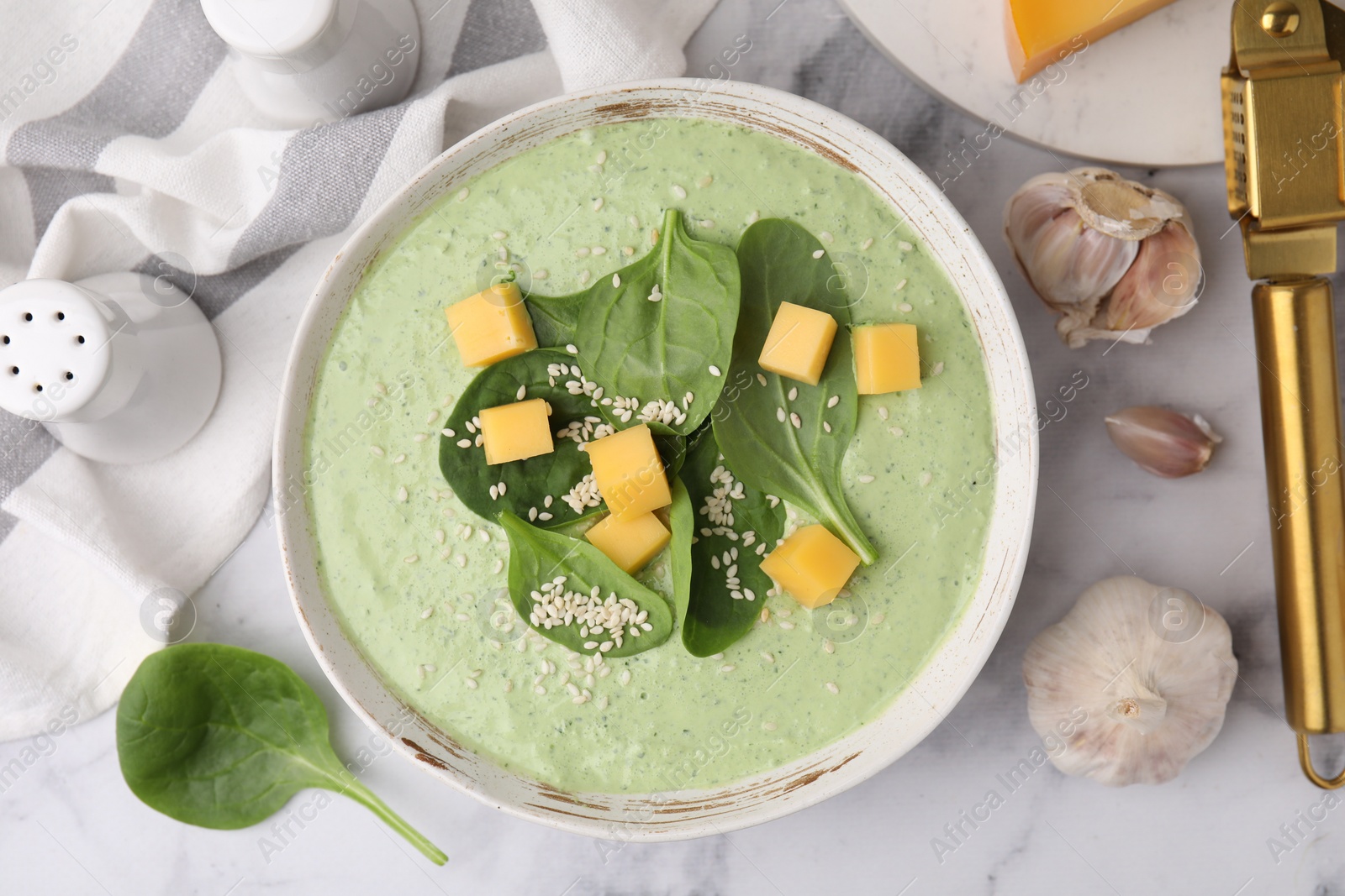 Photo of Delicious spinach cream soup with cheese and sesame seeds in bowl on white marble table, flat lay