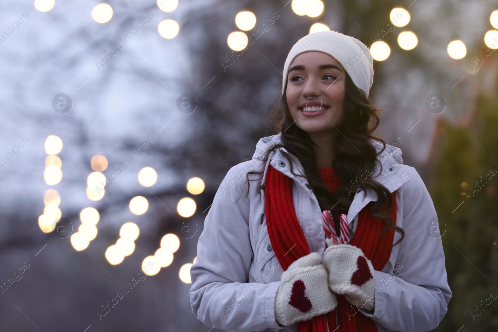 Photo of Happy young woman with candy canes on city street in evening. Christmas celebration