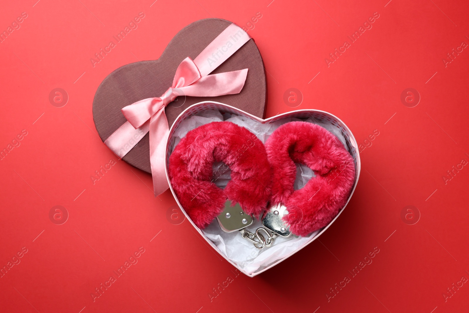 Photo of Gift box with furry handcuffs on red background, flat lay