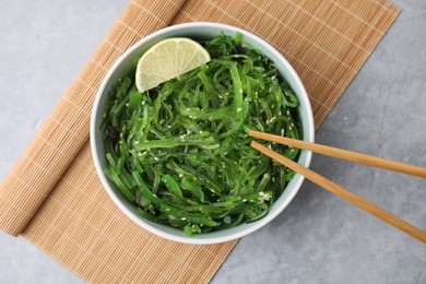 Photo of Tasty seaweed salad in bowl served on gray table, top view