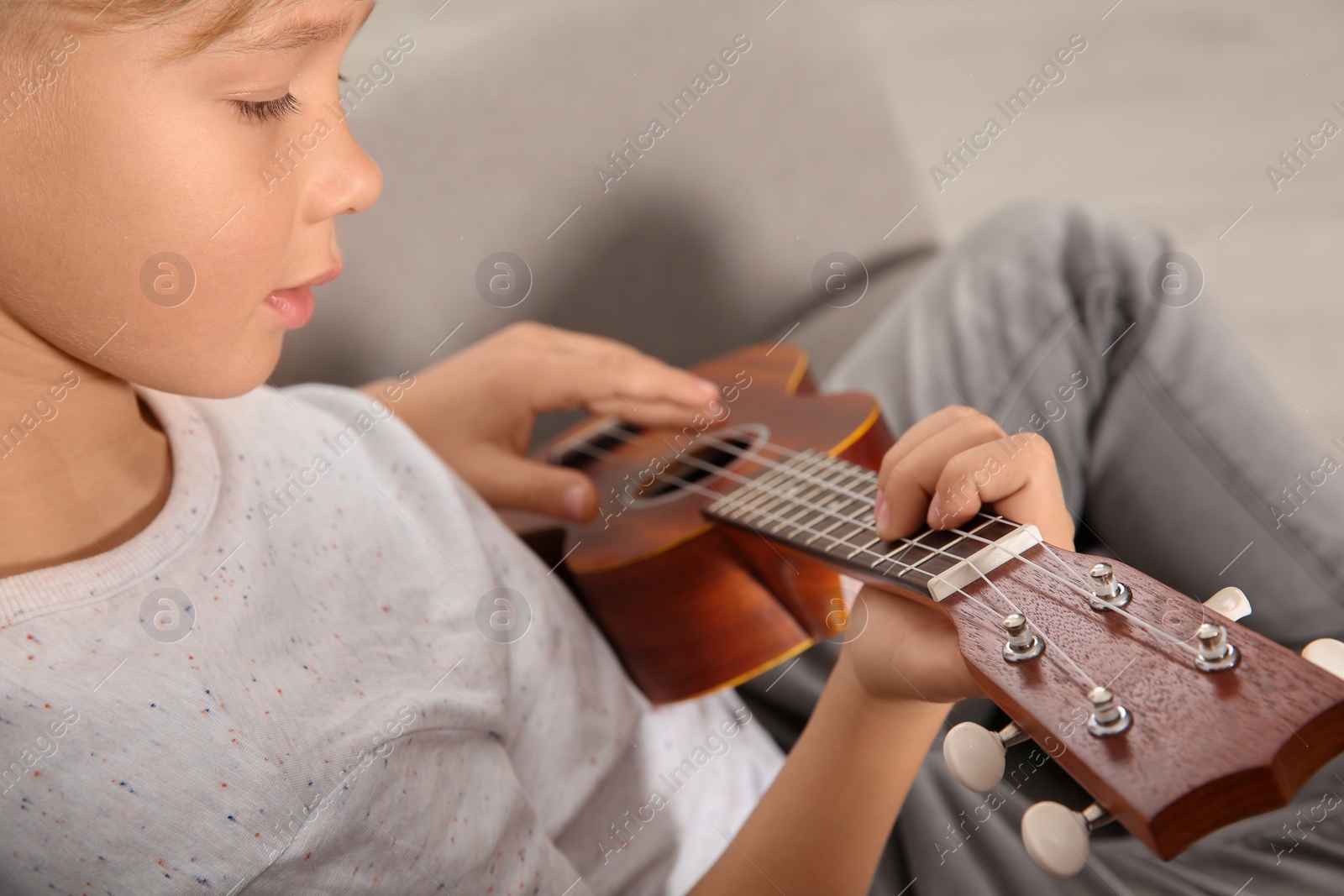 Photo of Little boy playing guitar on sofa in room, closeup