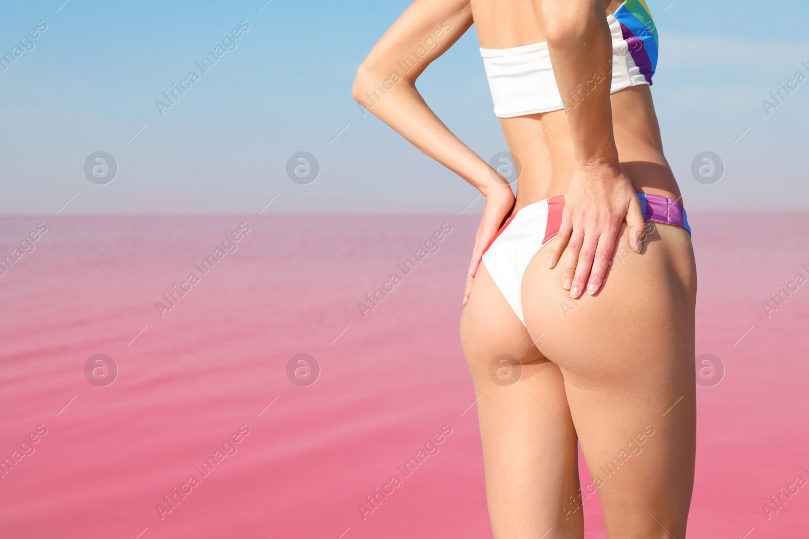 Photo of Beautiful woman in swimsuit posing near pink lake on sunny day, closeup