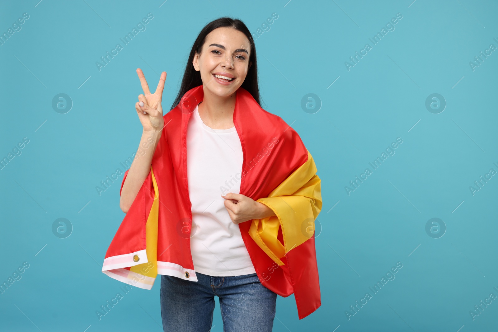 Photo of Happy young woman with flag of Spain showing V-sign on light blue background, space for text
